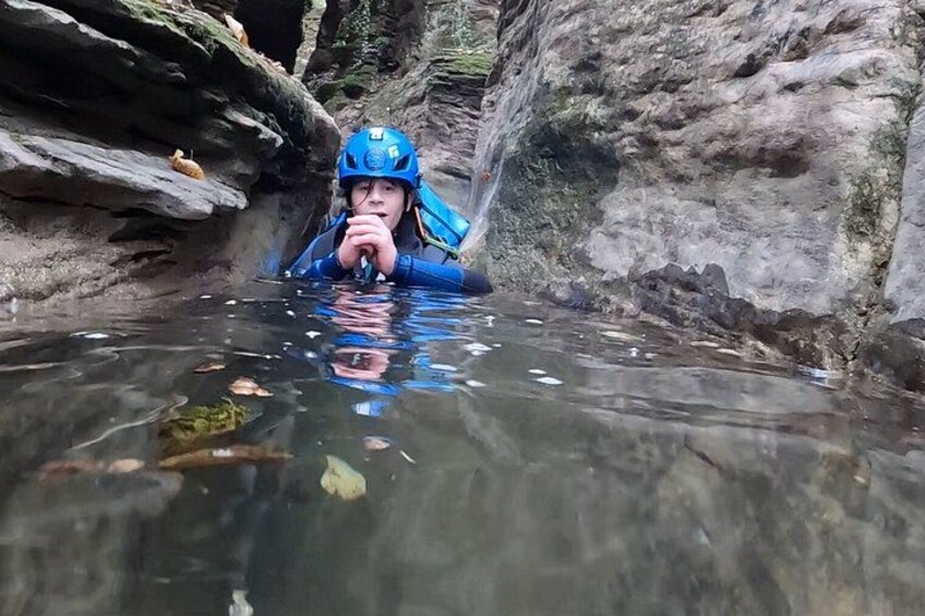 Una persona con botas azules y casco vadea por un estrecho canal de agua entre rocas. 5