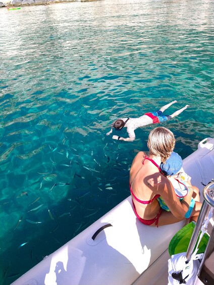 A person snorkeling in clear blue water, with a boat and another person in the background. 2