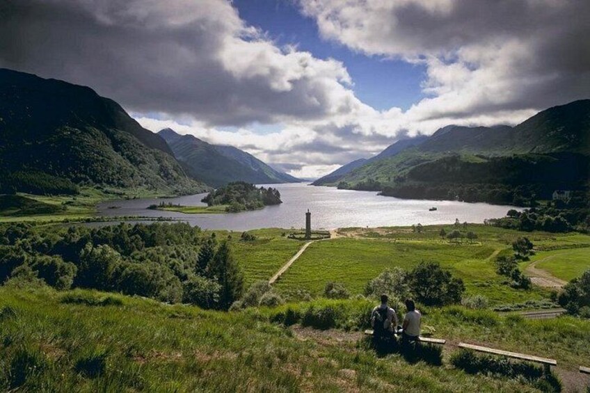 A mountainous landscape with a lake, a lighthouse, and a grassy area with people. 2