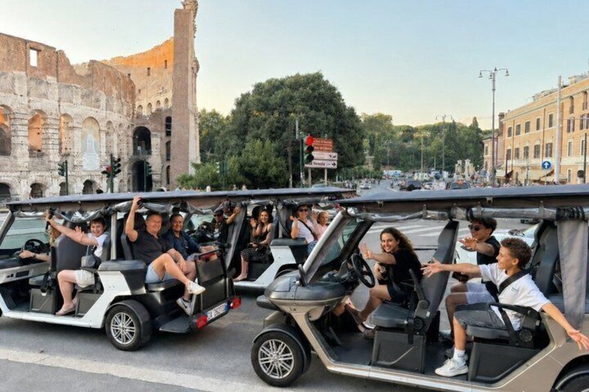 A group of people on a golf cart driving through a city street with historical buildings in the background. 1
