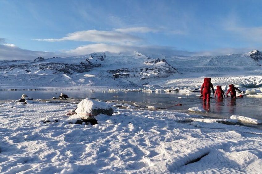 A snowy landscape with a group of people in red suits standing by a frozen lake. 3