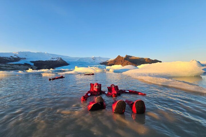 A group of people in red gear floating on ice in a frozen landscape with mountains in the background. 4