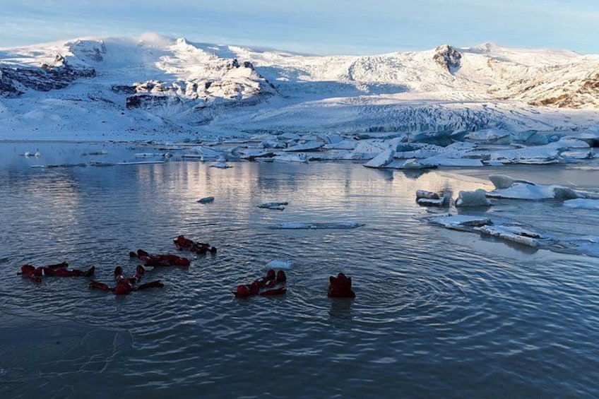 Un grupo de personas en kayaks rojos sobre un lago helado, rodeado de montañas nevadas. 2