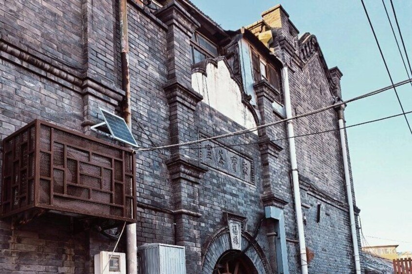 A historic brick building with a large arched entrance and a wooden structure on the left. 3