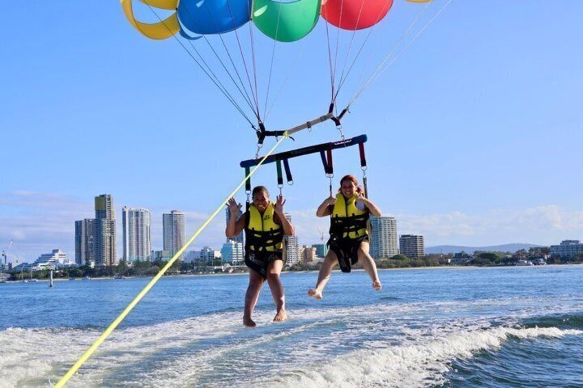 Two people parasailing over water with a city skyline in the background. 3