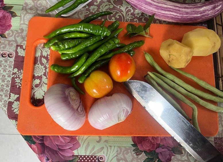 A cutting board with green chili peppers, tomatoes, onions, and a knife. 3