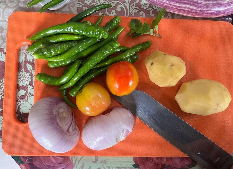 A cutting board with green chili peppers, a tomato, onions, and a knife. 4