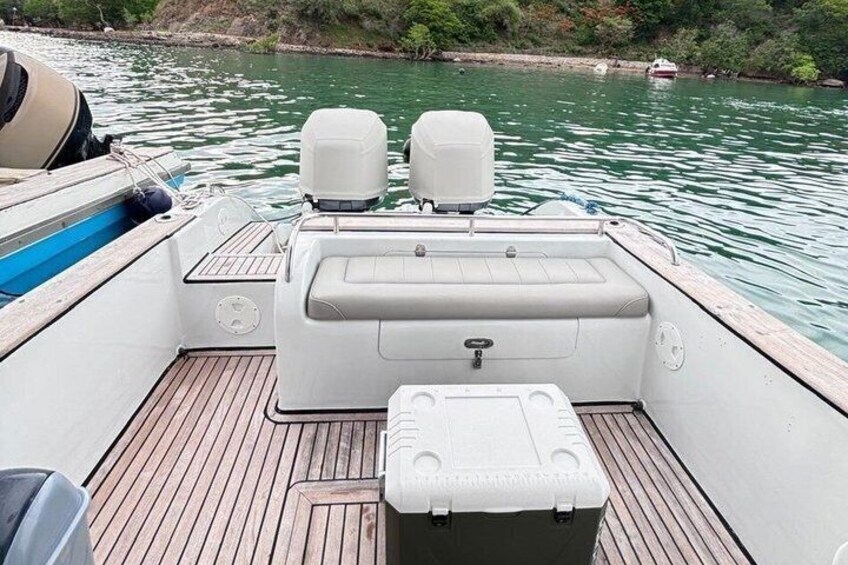 A boat's deck with a cushioned seating area, a storage box, and a steering wheel. 4