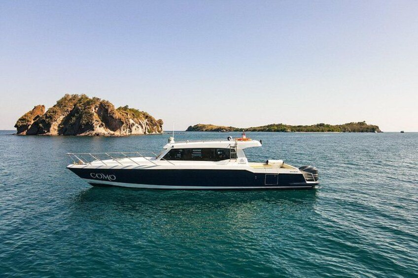 A black and white boat named 'COMO' on calm waters with rocky islands in the background. 1
