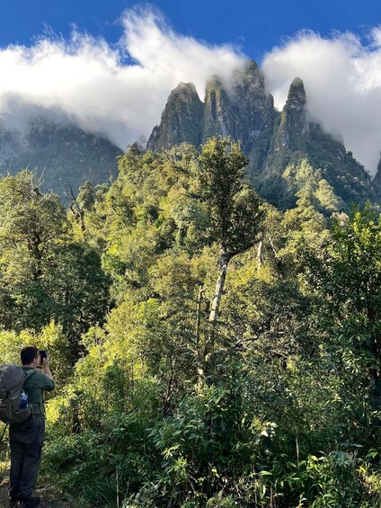 A hiker taking a photo of a mountain range with lush greenery and clouds. 1