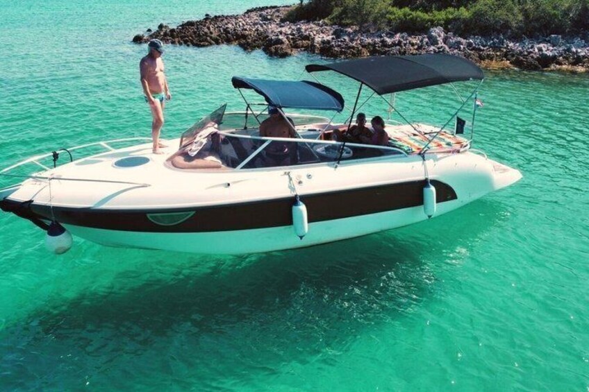 A small motorboat with a canopy, a person standing on the bow, and calm turquoise water. 2