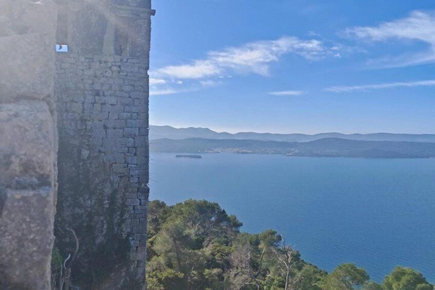 A stone wall overlooking a calm sea with distant mountains under a clear sky. 5