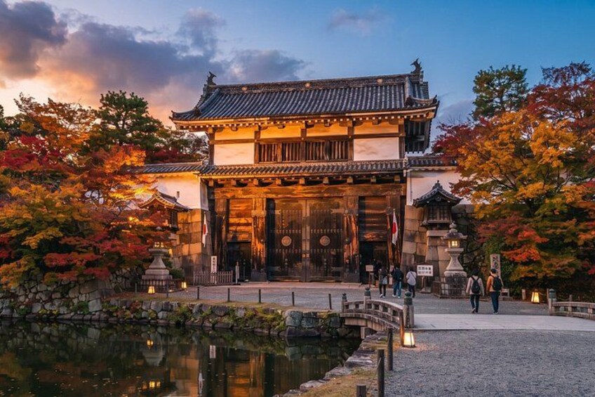 En traditionell japansk byggnad med ett tak täckt av tegelpannor, omgiven av träd i höstfärger och en lugn vattenyta. 3