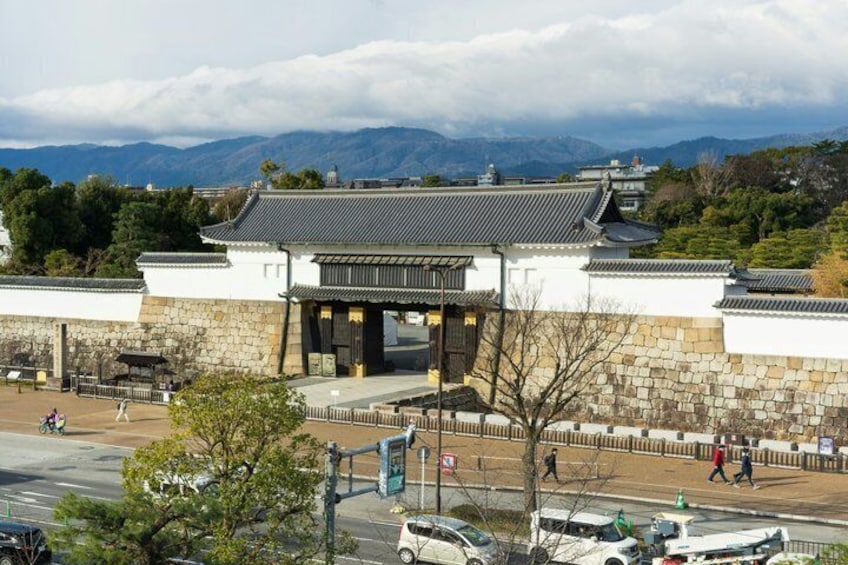 Ein traditionelles koreanisches Tor mit Steinmauern und einem Ziegeldach, umgeben von einem Park mit Bäumen und Blick auf ferne Berge. 5