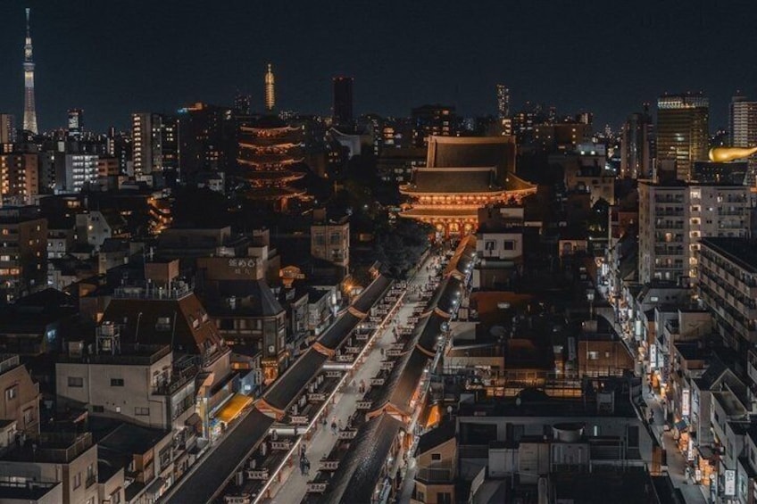 A nighttime cityscape with illuminated buildings, a prominent tower, and a traditional structure with a curved roof. 2