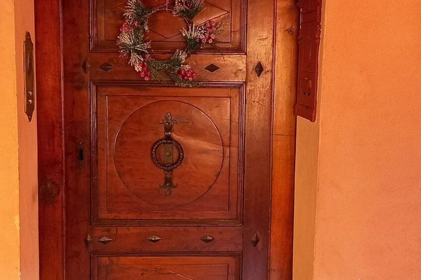 A wooden door with a circular handle and a wreath above it. 2