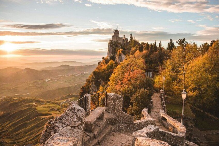 A historic castle on a hilltop with autumn foliage, surrounded by stone walls and a pathway. 5