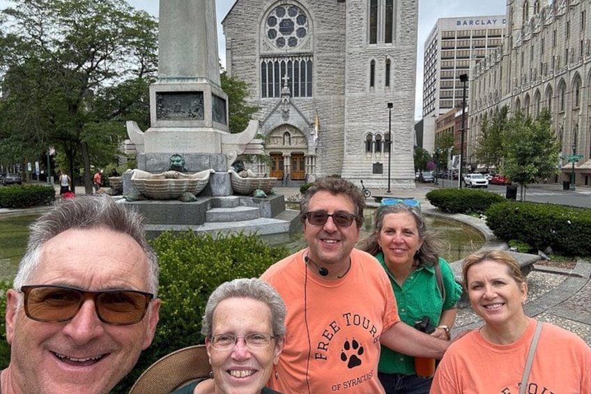 A group of people in front of a church with a large steeple and a memorial fountain. 3