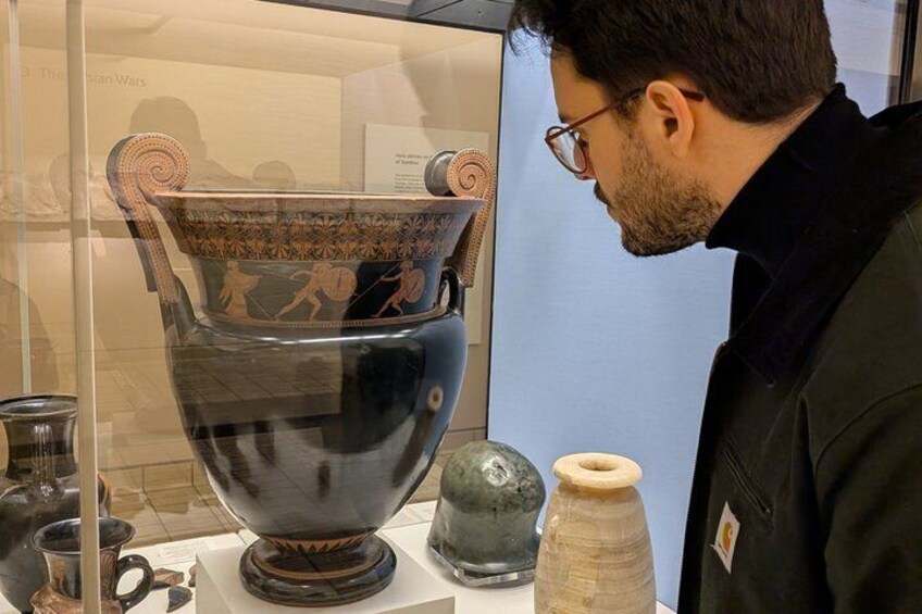 A person examining a large ancient Greek vase with red-figure painting in a museum. 4