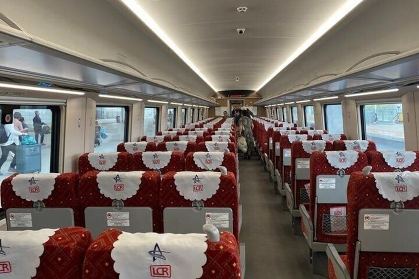 A train interior with rows of seats, each with a red and white cover and a logo on the backrest. 2
