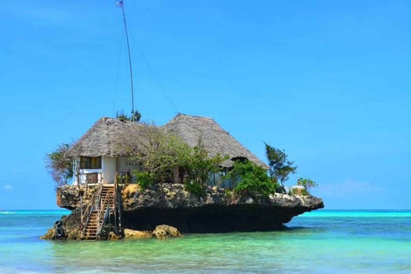 A thatched-roof house on a rocky outcrop surrounded by clear turquoise water. 1