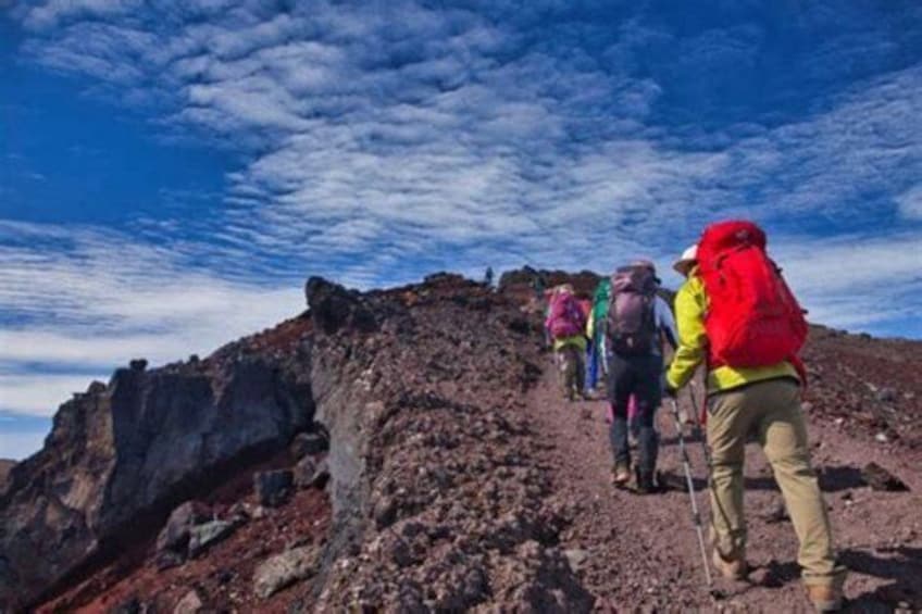 En grupp vandrare tar sig uppför en bergig stig medan himlen är delvis molnig. 5