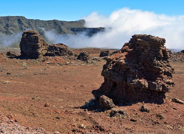 A rocky landscape with layered rock formations and steam rising from the ground. 5