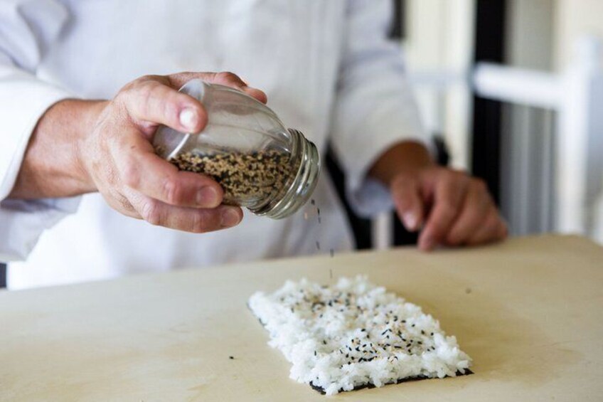 A person holding a glass jar of seeds, about to sprinkle them onto a white surface. 3