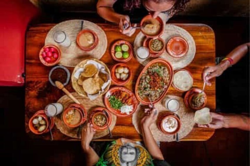 A group of people around a wooden table with various dishes and bowls of food. 3