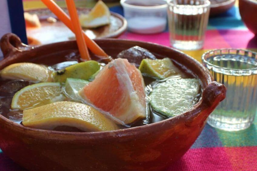 A clay pot with a piece of salmon, lemon slices, and green vegetables. 4