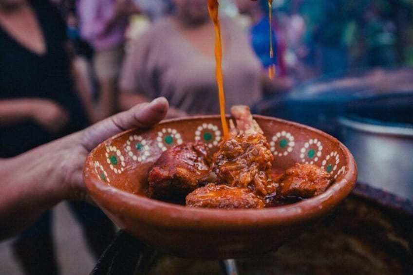 A hand holding a clay bowl with a sauce being poured over meat. 2