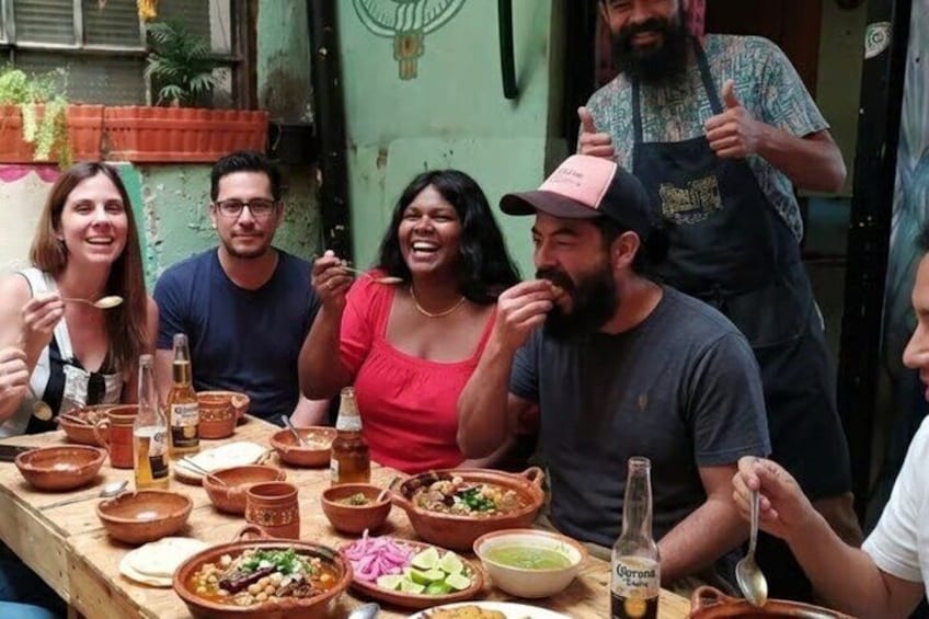A group of people dining outdoors with various dishes and a bottle of beer on the table. 1