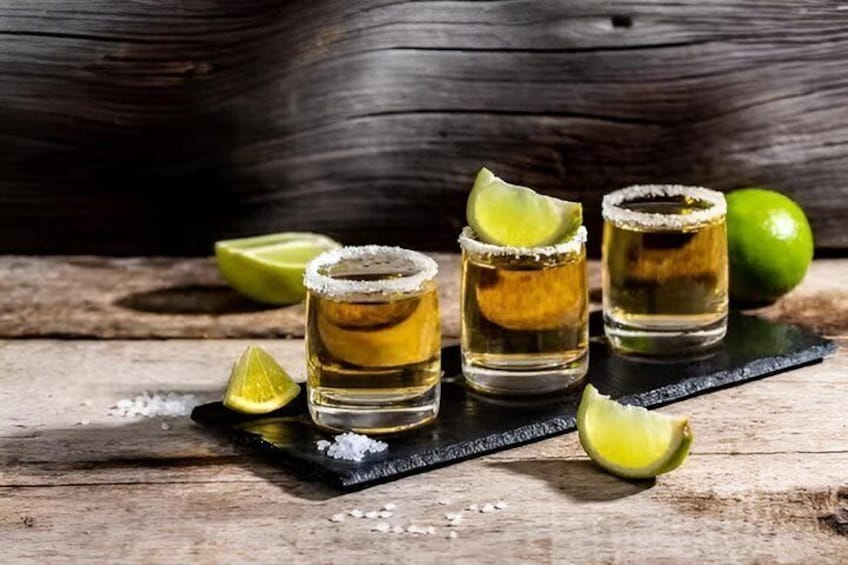 Three shot glasses with a salted rim, lime wedges, and a wooden surface. 5