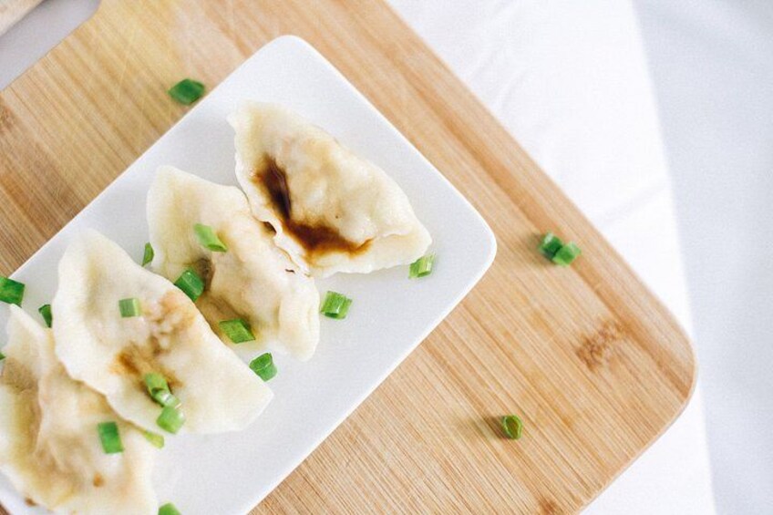 A plate of dumplings garnished with chopped green onions on a wooden cutting board. 2