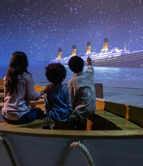 Three people sitting on a boat, looking at a ship on the water. 2