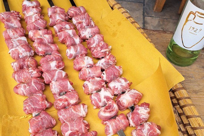 Raw meat skewers on a yellow surface with a bottle of green liquid beside them. 3