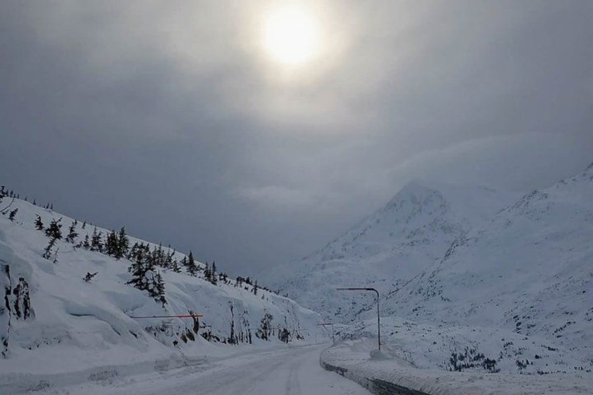 A snow-covered mountain road with a clear sky and a bright sun. 4
