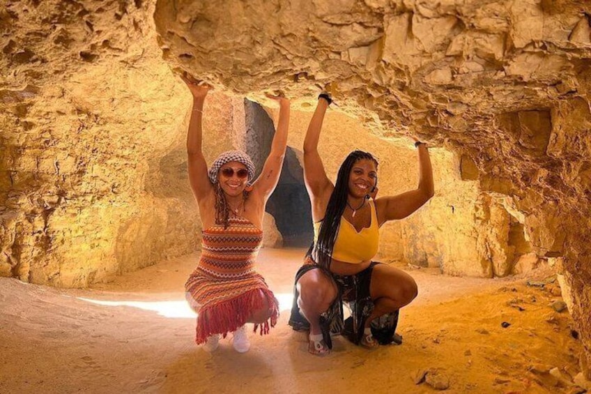 Two people in a cave with rocky walls and a sandy floor. 2