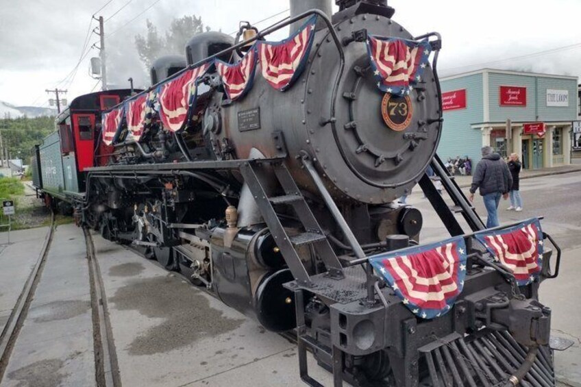 A steam locomotive with American flags, number 73, parked on tracks with a building in the background. 2