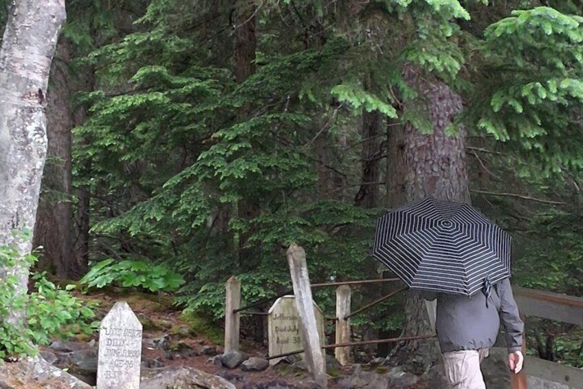 A person walking in a forested area with a striped umbrella, a wooden signpost, and a stone marker. 2