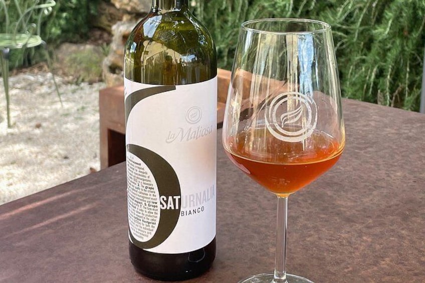 A bottle of SATURNALIO BLANCO wine and a glass of red wine on a table. 2