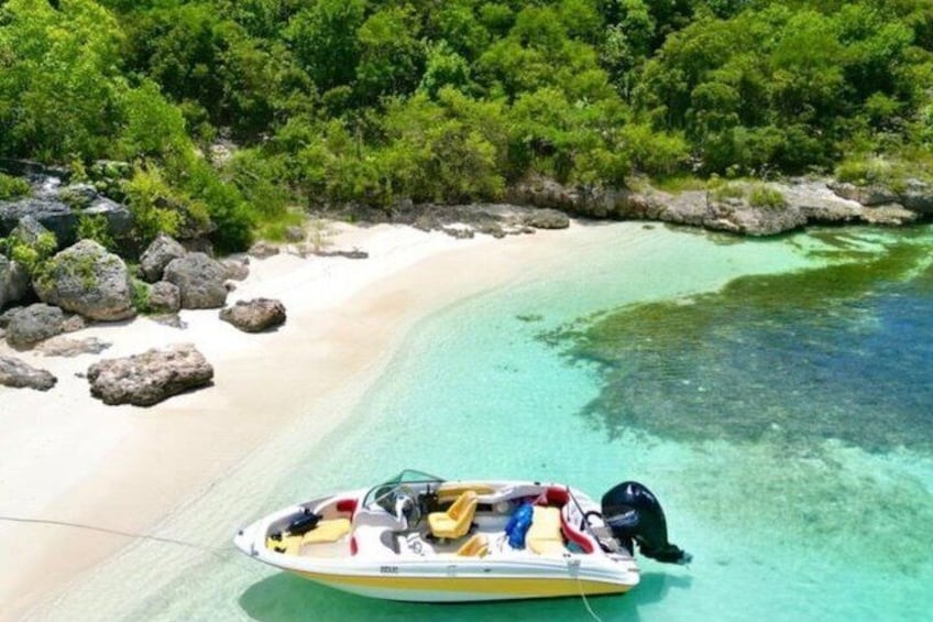 A boat on a clear turquoise beach with white sand and dense green foliage in the background. 2