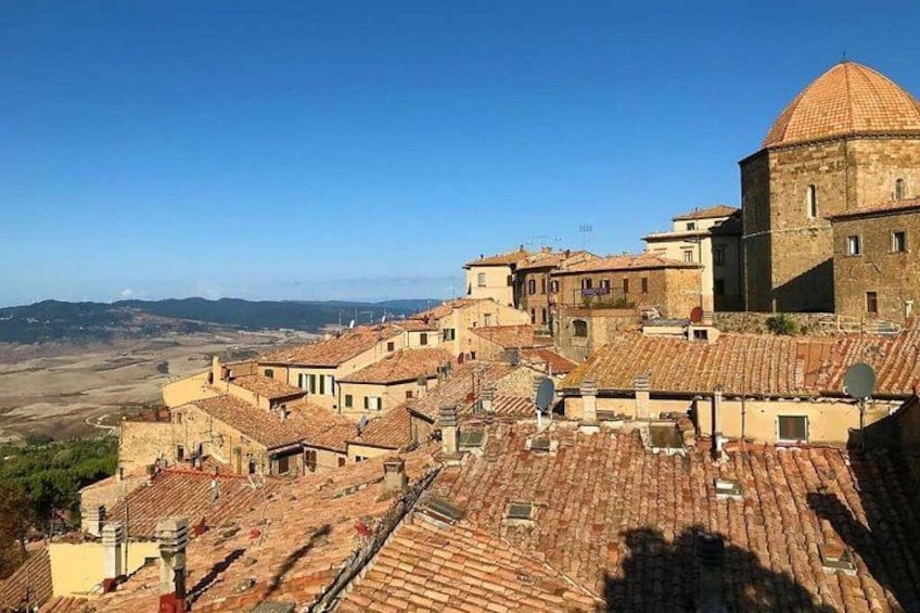 Un pueblo con edificios de tejados de terracota, una estructura cúpula destacada y un paisaje montañoso al fondo. 5