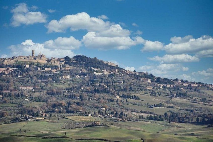 Un paisaje montañoso con un castillo histórico en la cima, campos ondulantes y edificios dispersos. 2