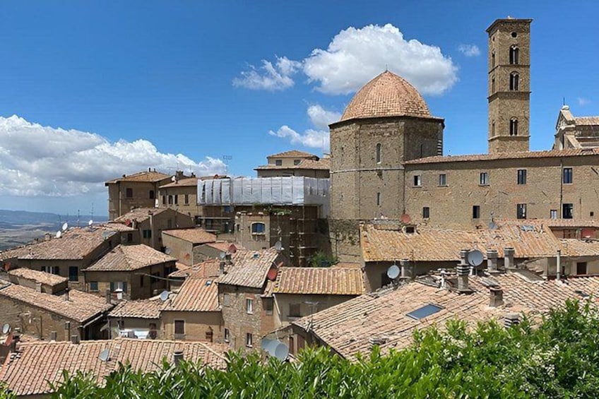 A historic town with terracotta-roofed buildings, a prominent church with a dome, and a tower. 3