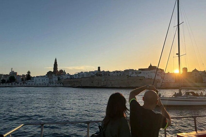 A sunset over a coastal city with a prominent tower and a sailboat in the foreground. 2