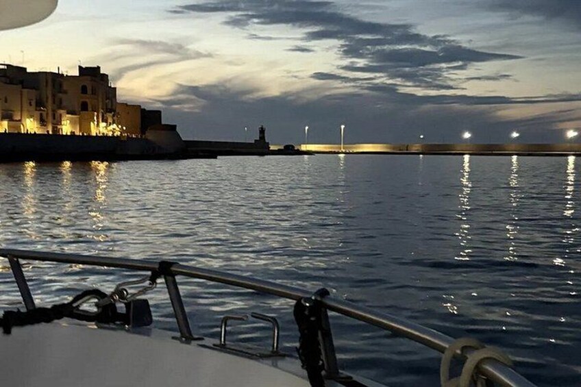 Una barca su acque calme, con uno skyline urbano e un faro in lontananza. 2