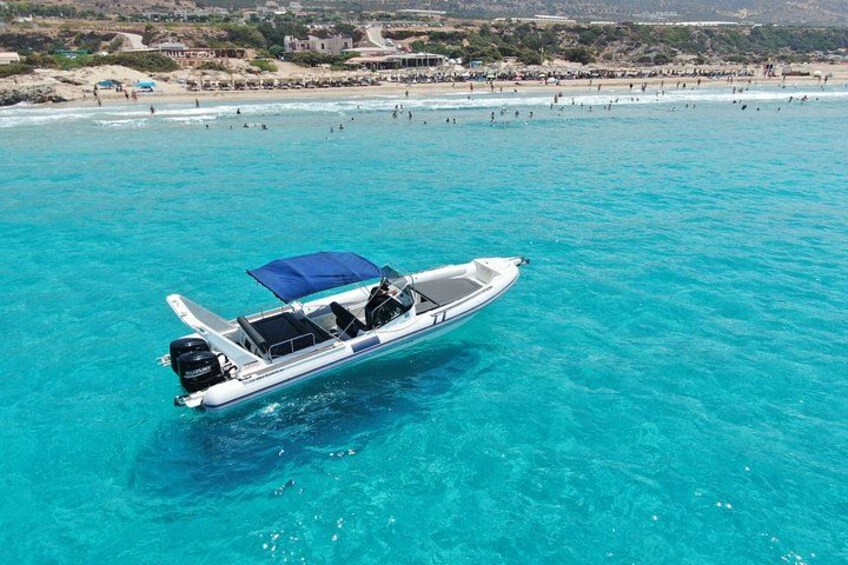 A boat on turquoise water with a beach and buildings in the background. 4