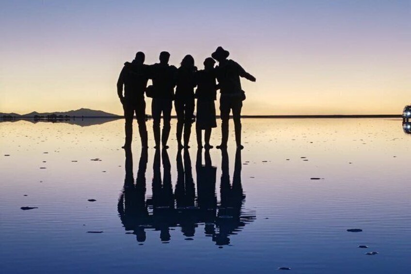 A group of people standing on a reflective water surface at sunset with mountains in the background. 5