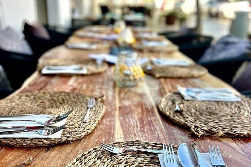 A long wooden table with woven placemats, cutlery, and a glass centerpiece. 3